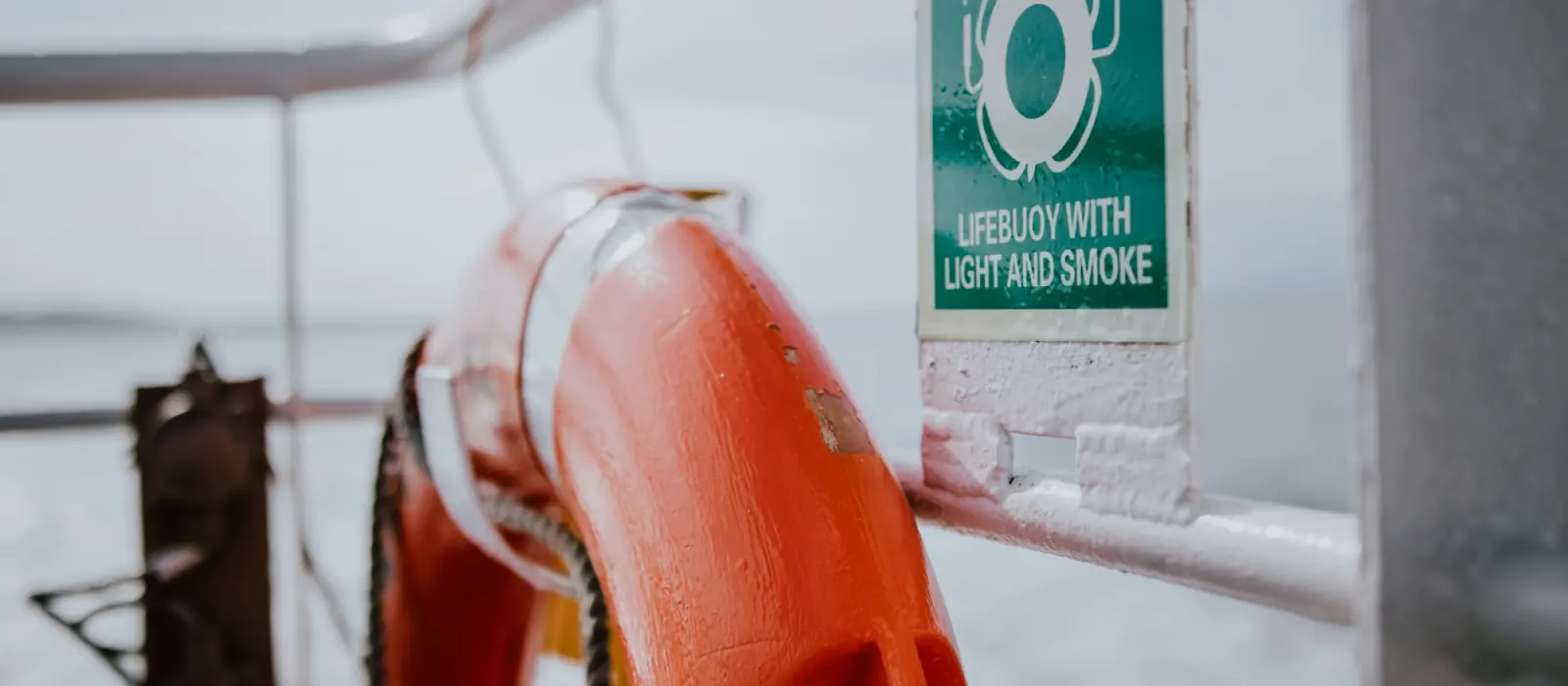 A lifebuoy on a ship's rail beside its IMO sign: lifebuoy with light and smoke