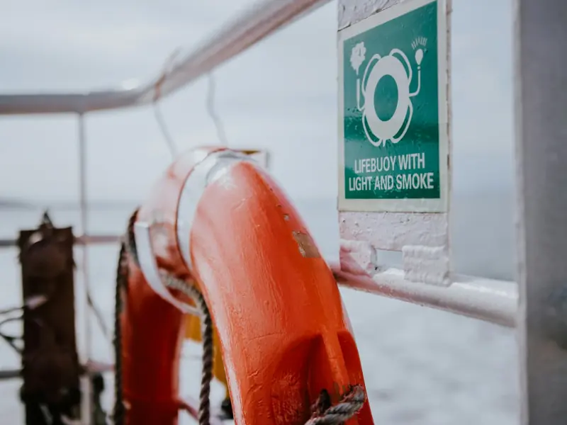 A lifebuoy on a ship's rail beside its IMO sign: lifebuoy with light and smoke